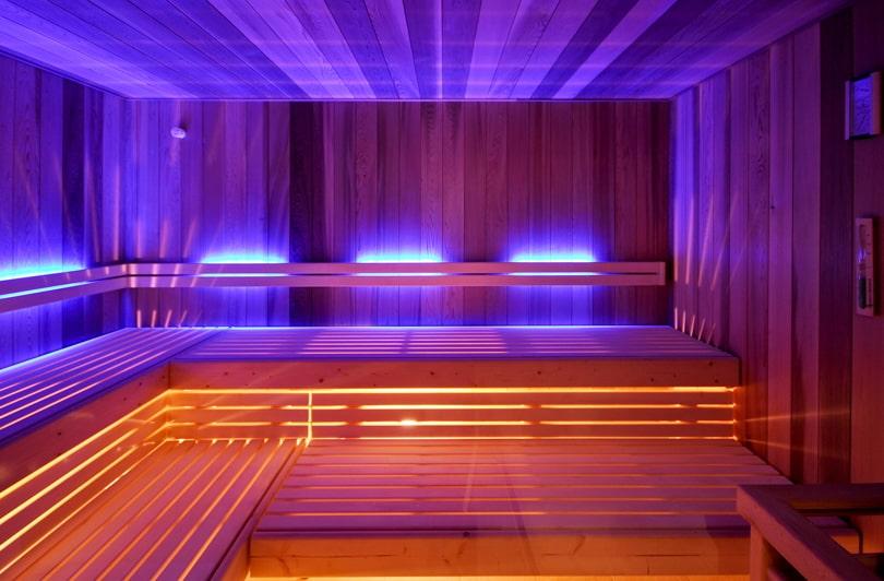 Wooden sauna interior with atmospheric blue and warm orange lighting in the eco-spa area of the SANDglow boutique hotel. Benches line the walls, creating a calm and inviting atmosphere.