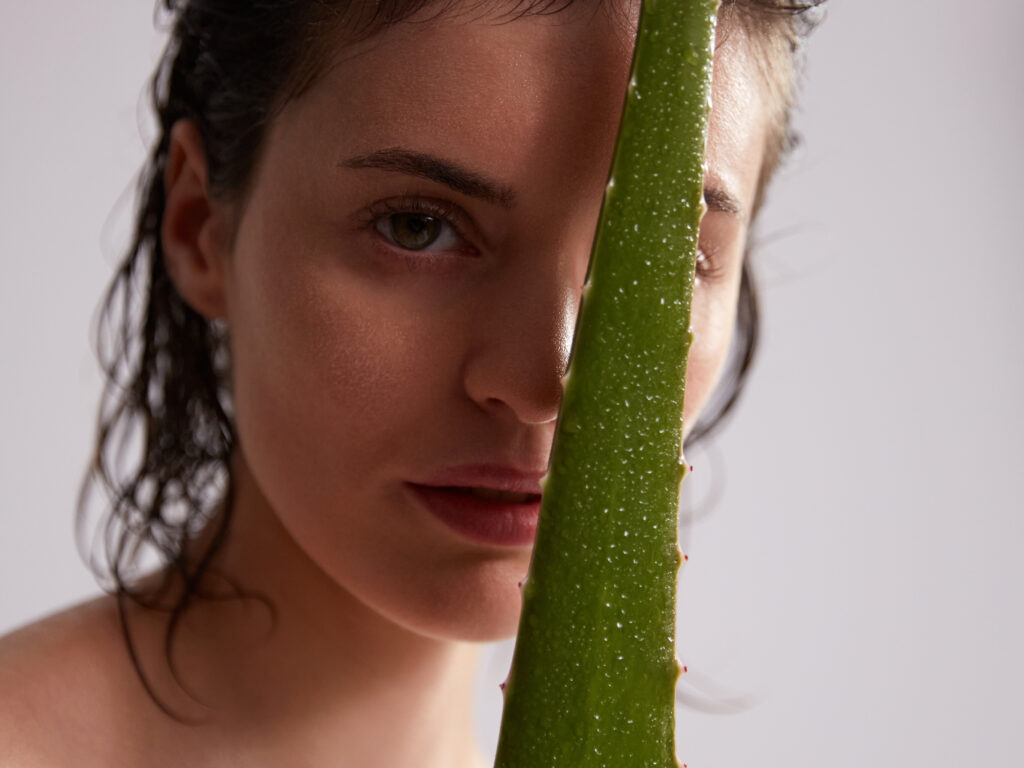 Eine Frauschaut hinter einer Aloe Vera Pflanze