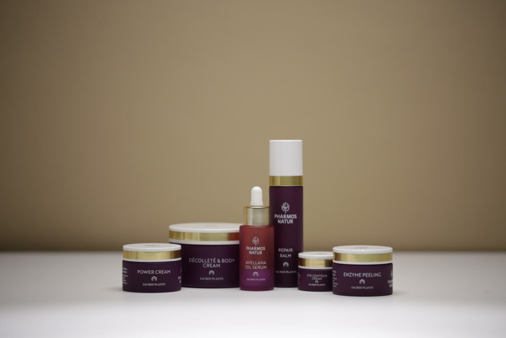 Eine Kollektion dunkelroter Hautpflegeprodukte von Pharmos Natur, ordentlich angeordnet vor einem sanften beigen Hintergrund, vermittelt ein Gefühl von Luxus und Wohlbefinden.