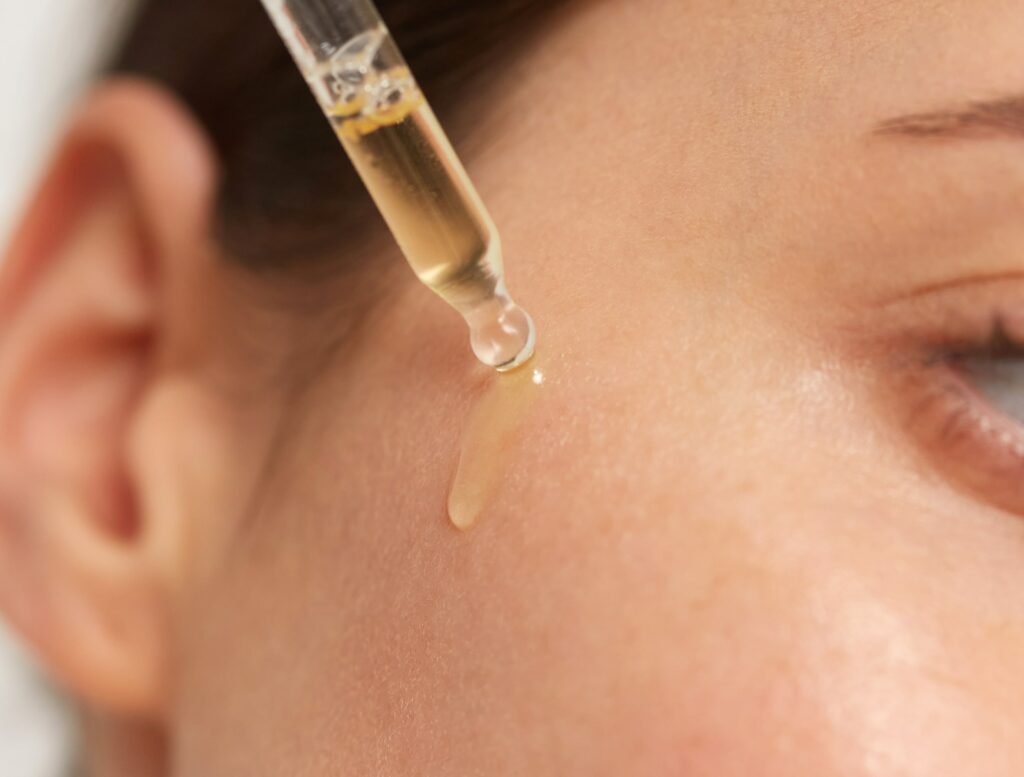 Nahaufnahme einer Pipette, mit der Öl von Pharmos Natur auf die Wange einer Person aufgetragen wird, um die Hautpflege-Routine zu veranschaulichen. Das Bild vermittelt ein Gefühl von Pflege und Wohlbefinden.