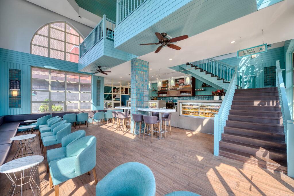 Bright, airy café with turquoise décor, comfortable seating, stairs, high ceiling fans, and large windows. Warm, inviting atmosphere at the Turkish resort Megasaray Club Belek.