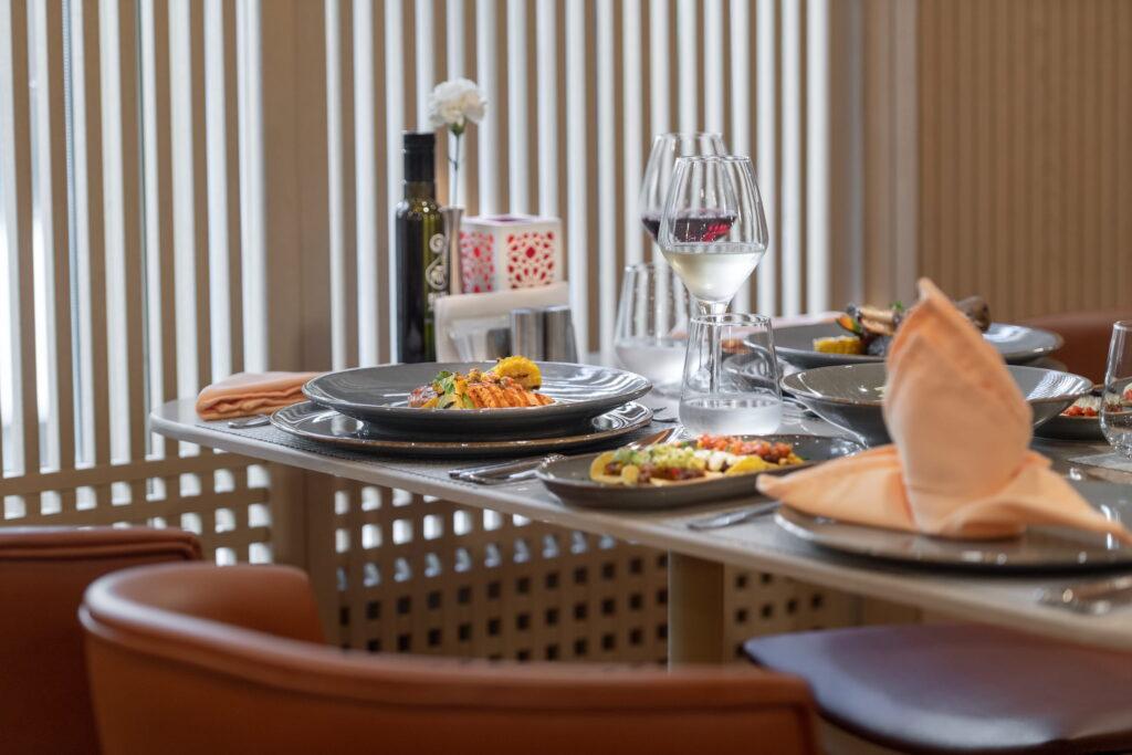 Elegant restaurant table at Megasaray Club Belek, a sustainable resort in Antalya, Turkey, set with gray plates featuring artfully arranged dishes, a wine glass, folded napkin, and soft lighting that create a sophisticated atmosphere.