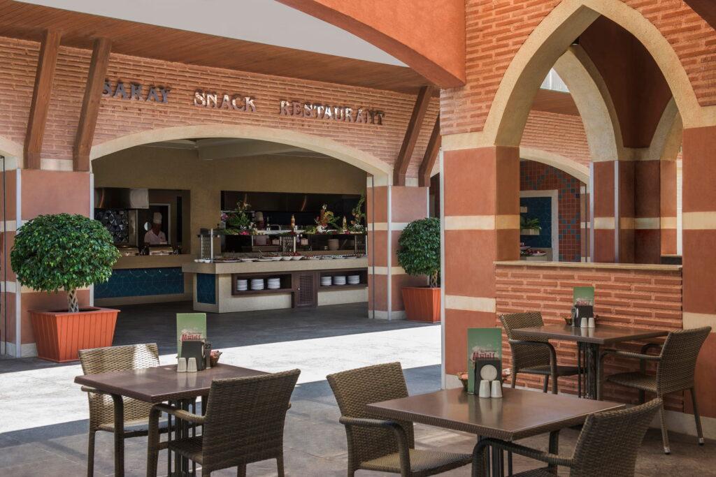 Outdoor restaurant with Mediterranean flair at the Turkish all-inclusive resort Megasaray Club Belek. With brick arches and neatly arranged tables with wicker chairs. Lush potted plants create a welcoming atmosphere.