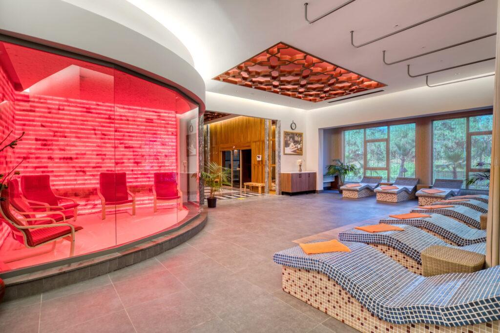 Modern salt lounge at the GSTC-certified Megasaray Club Belek resort in Turkey, featuring a red-lit sauna and comfortable tiled loungers. Large windows offer views of the garden and create a calm, relaxed atmosphere.
