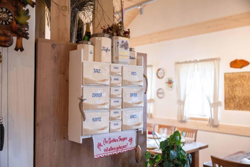 Wall-mounted antique spice cabinet in the Dorfschenke restaurant at Ebner 1822 in Austria with labeled drawers for salt, rice, sugar, flour, and coffee. Rustic room background with wooden furniture and soft lighting.