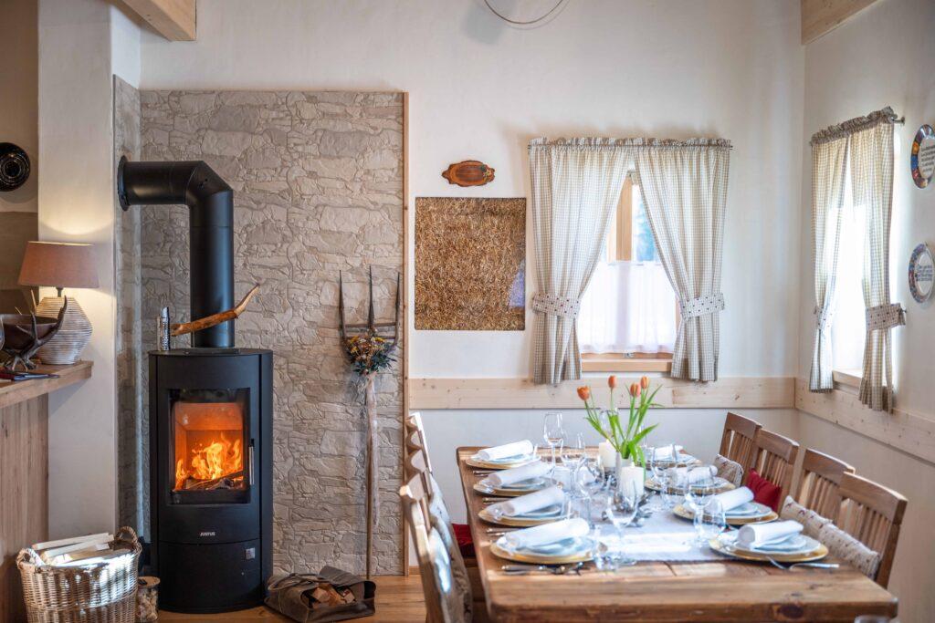 Cozy dining room in the Dorfschenke restaurant in Ebner 1822, Austria, with a wooden table for eight people, set with plates, glasses, and a vase of tulips. A lit wood stove adds extra warmth to the rustic decor.