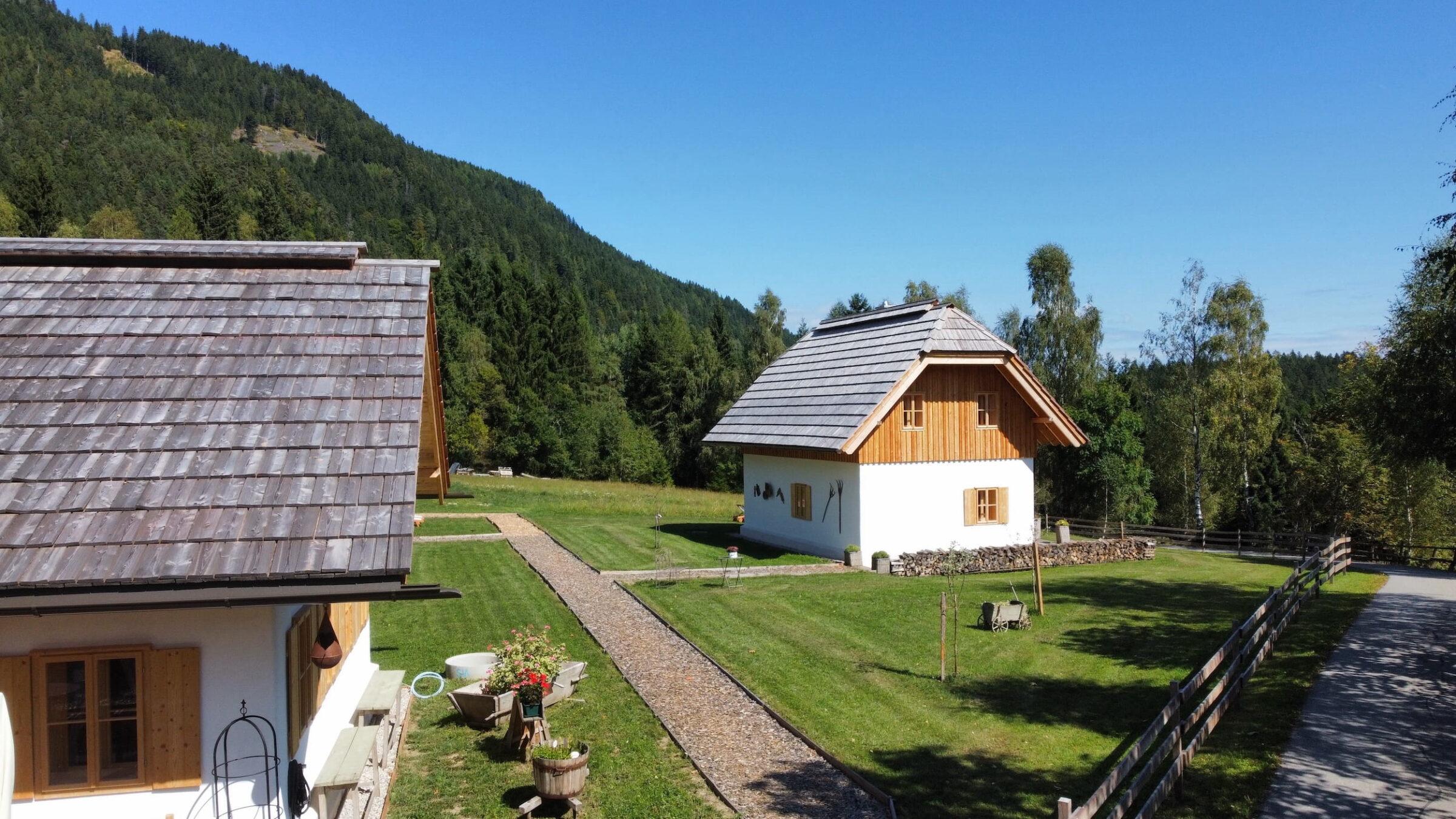 Two rustic wooden holiday homes with sloping roofs are nestled in lush green countryside, surrounded by dense forests and clear blue skies, exuding tranquility. Ebner 1822 in Carinthia, Austria