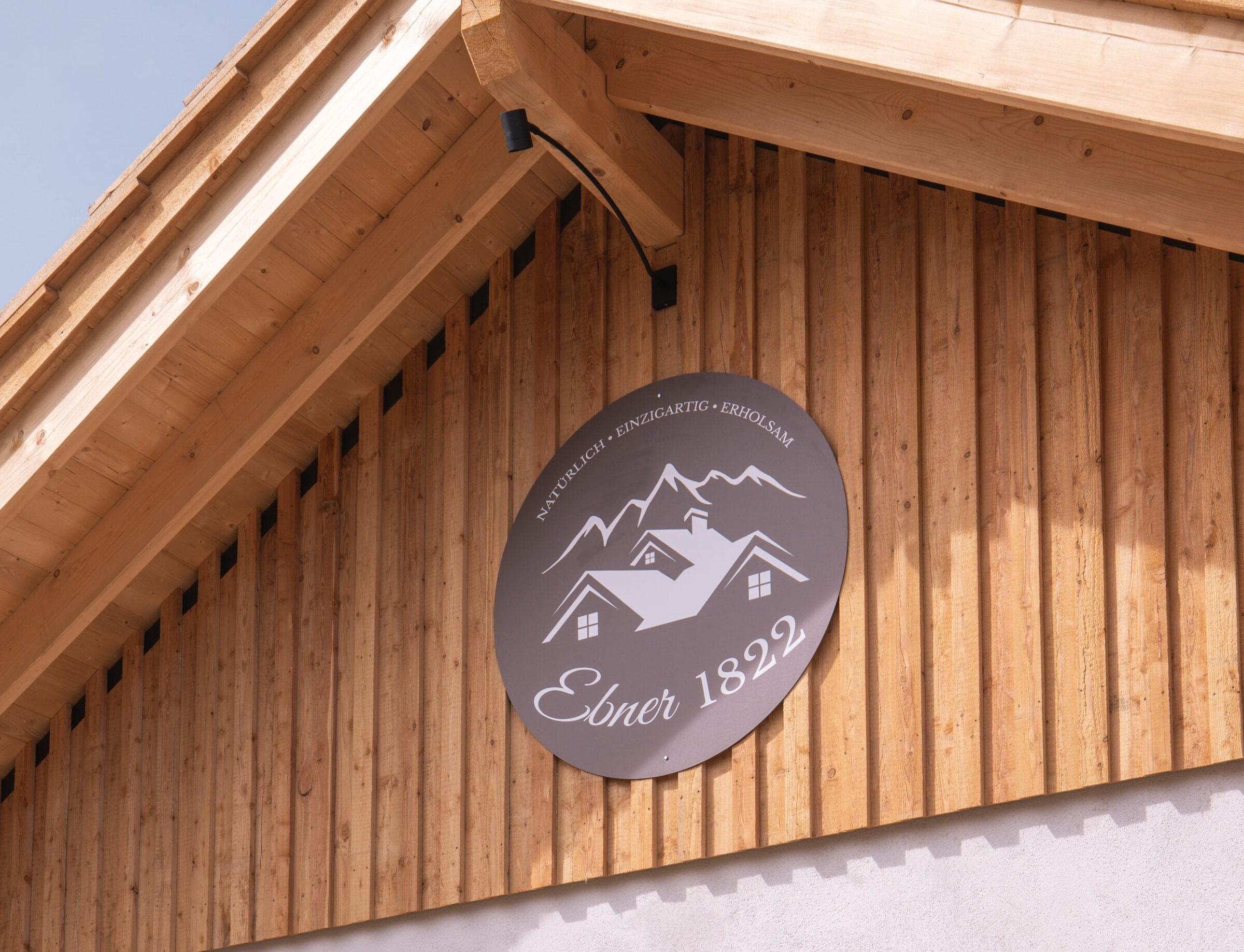 Wooden facade with a round sign bearing the inscription “Ebner 1822” and mountain and house motifs, conveying a rustic, traditional flair.
