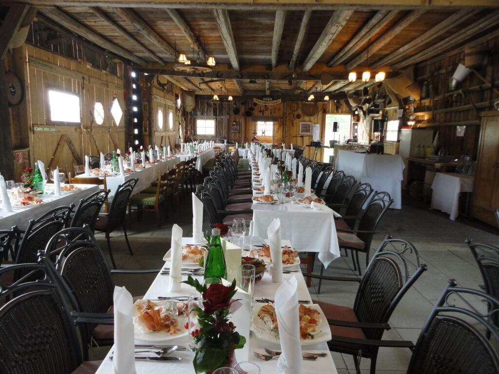 A rustic dining room in the sustainable Hotel Schloss Lerchenhof in Carinthia for an event, with long tables set with white tablecloths, folded napkins, starter plates, and chic glasses. The warm lighting and wooden decorations create a cozy atmosphere.