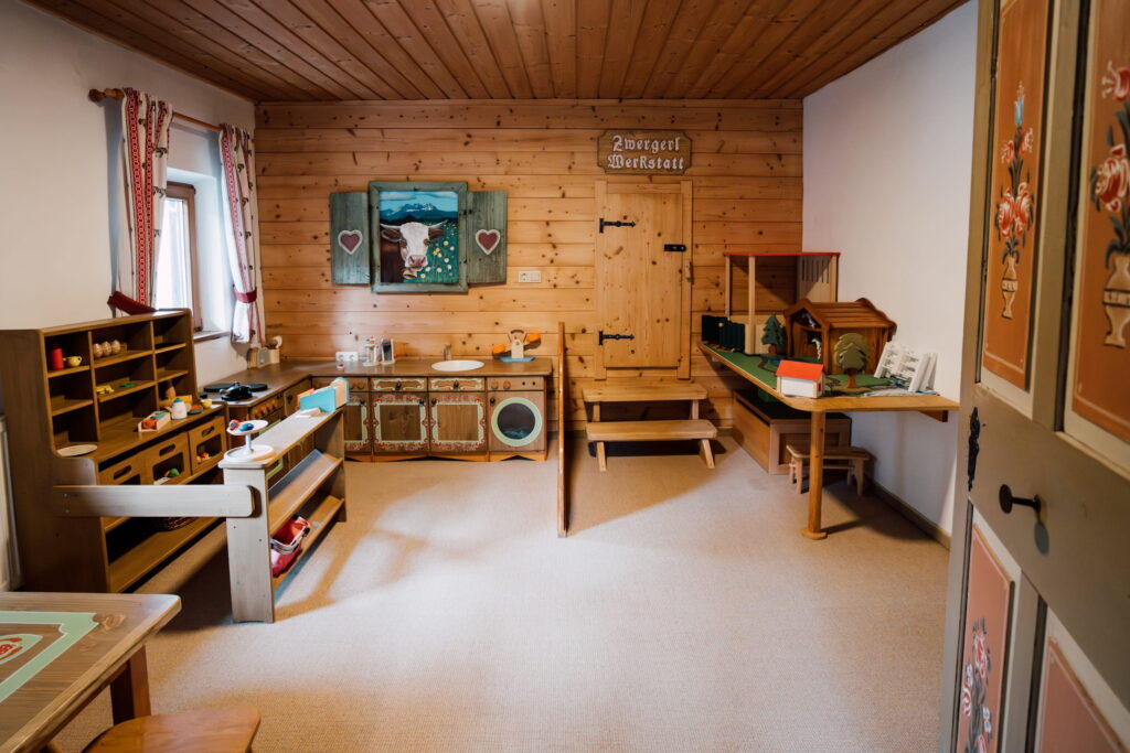 Kinderspielküche und Spielzeugregale in einem Holzraum mit bemalten Türen und einem Bild einer Kuh an der Wand im Bio- und Wellnessresort Stanglwirt in Tirol