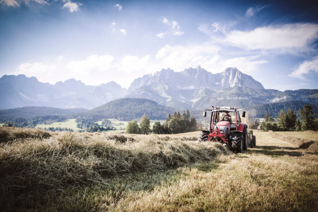 Traktor bei der Heuernte auf einer Wiese vor den Bergen des Wilden Kaisers in Tirol