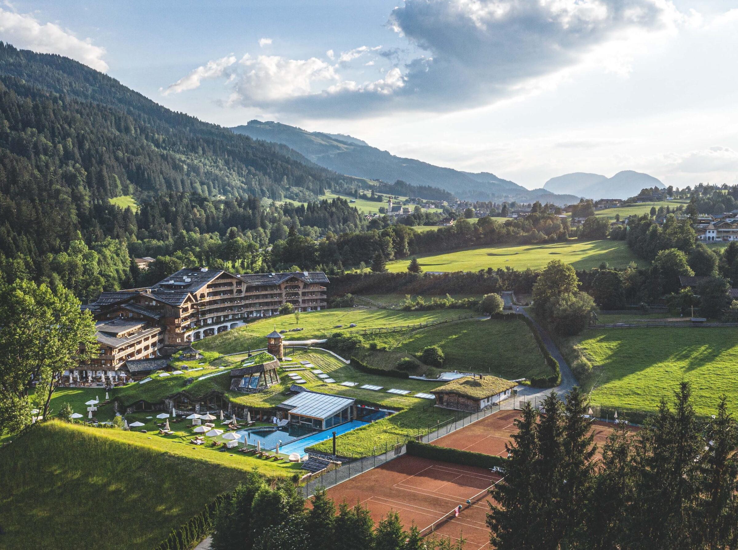 Luftaufnahme des Bio- und Wellnessresorts Stanglwirt in Tirol mit umgebenen Wiesen, Tennisplätzen und bewaldeten Bergen des Kaisergebirges im Hintergrund