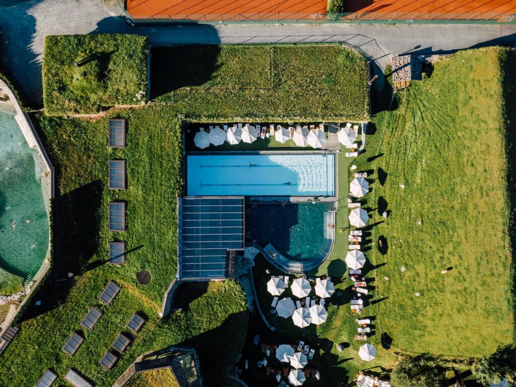 Luftaufnahme des Sportbeckens und Solepools im Bio- und Wellnessresort Stanglwirt mit umliegenden Liegen und Sonnenschirmen auf einer grünen Dachfläche