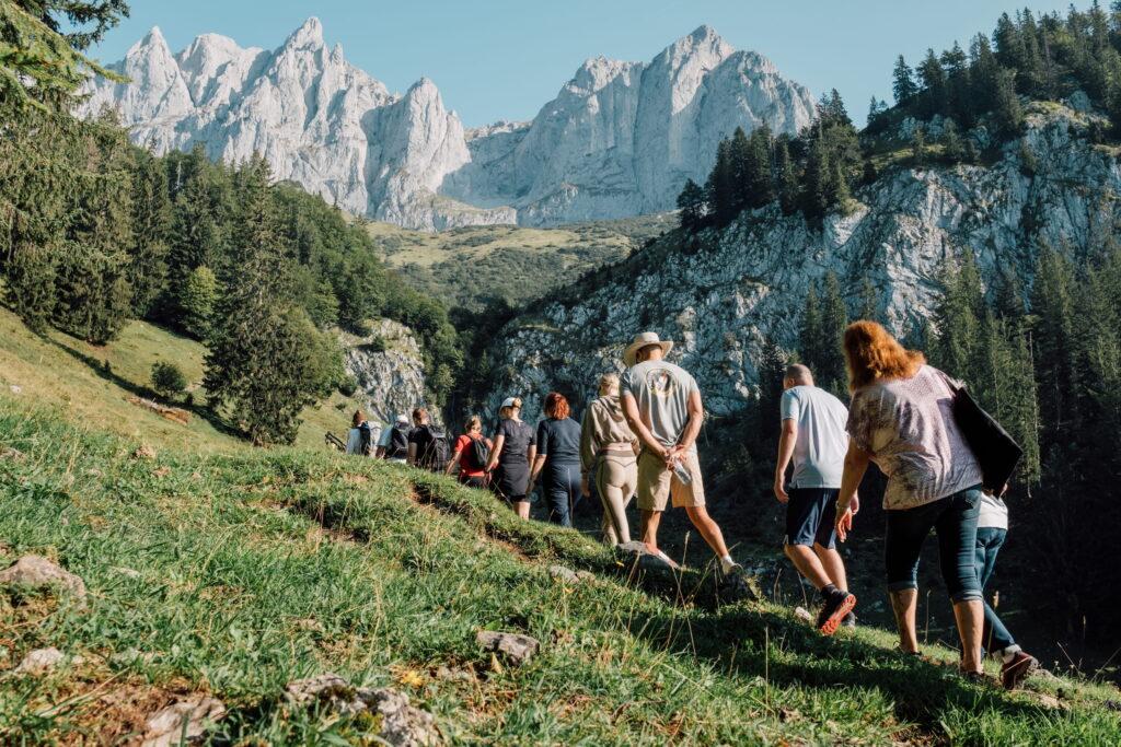 Gruppe von Wanderern auf einem grasbewachsenen Pfad vor steilen Felswänden und bewaldeten Hängen in den Tiroler Alpen