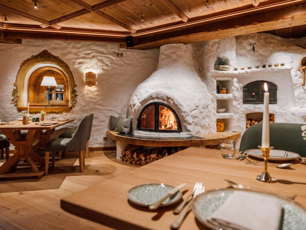 Rustikales Restaurantinterieur im Restaurant leni's im Stanglwirt mit runder, weiß verputzter Kaminöffnung, Holztischen, gepolsterten Stühlen und dekorativem Spiegel an der Wand