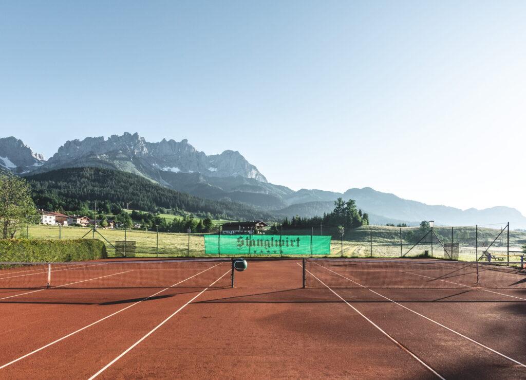 Tennisplatz mit rotem Sandbelag vor Bergkulisse des Wilden Kaisers im Bio- und Wellnessresort Stanglwirt in Tirol