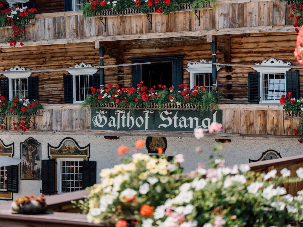 Traditioneller Gasthof Stanglwirt mit Holzfassade, Balkonen mit roten und weißen Blumen und schwarzen Fensterläden in Tirol