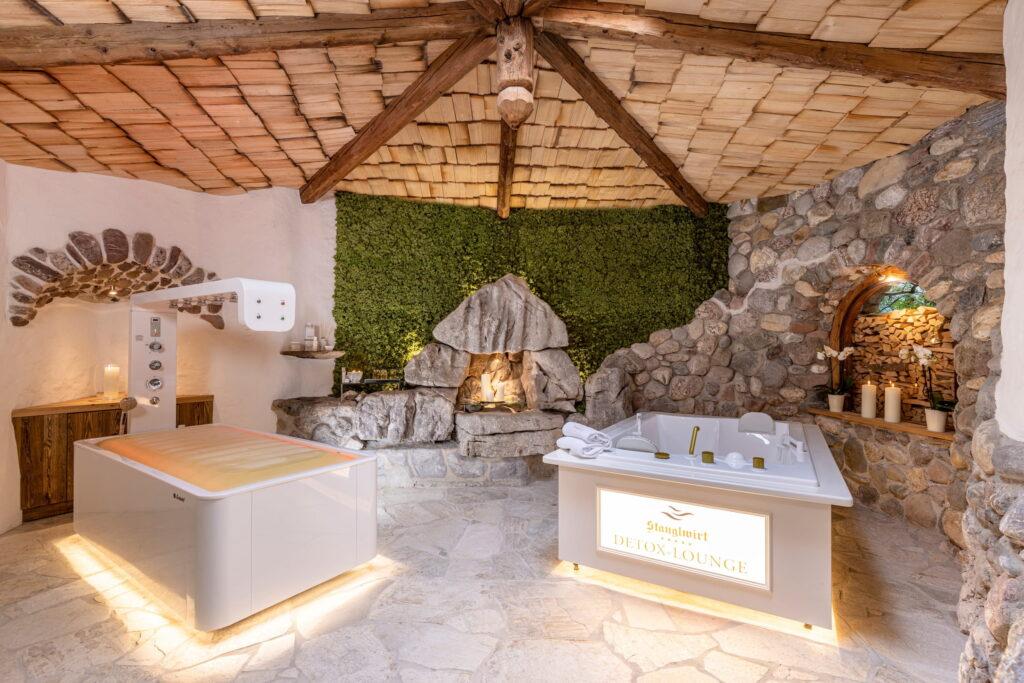 Wellnessraum mit zwei modernen Whirlpools, Natursteinwänden, Kamin und grüner Mooswand im Bio- und Wellnessresort Stanglwirt in Tirol