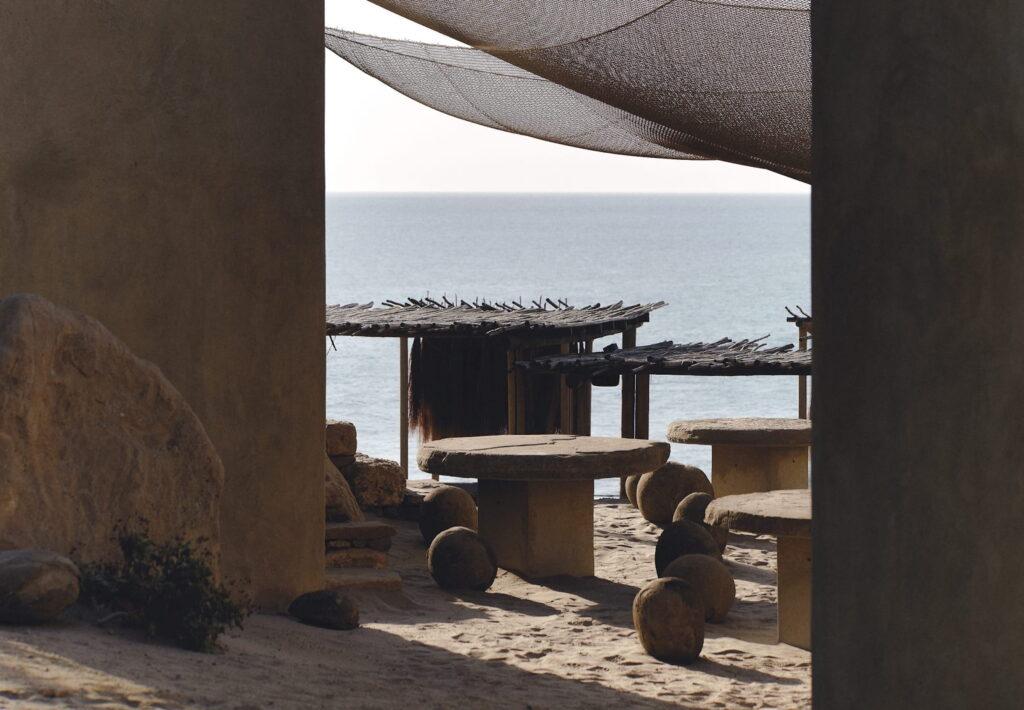 Außenbereich mit runden Steintischen und kugelförmigen Steinhockern unter einem schattigen Vordach mit Blick auf das Meer im Inkaterra Cabo Blanco