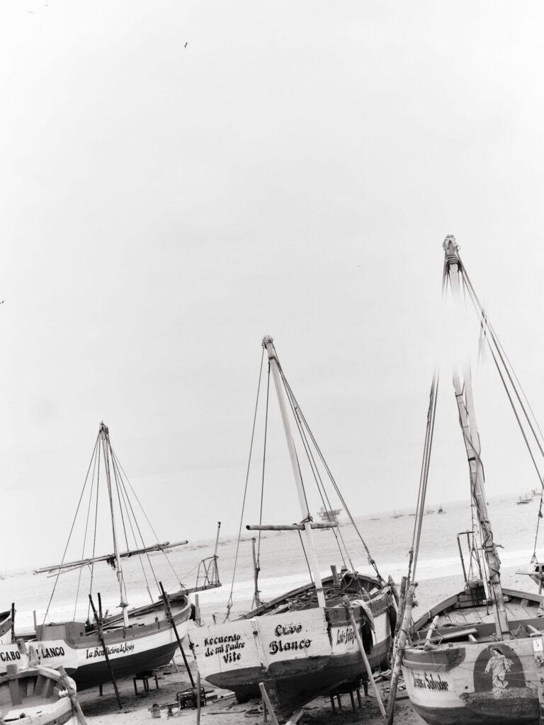 Eine Gruppe traditioneller Holzfischerboote mit hohen Masten, die an einem Strand vor Anker liegen