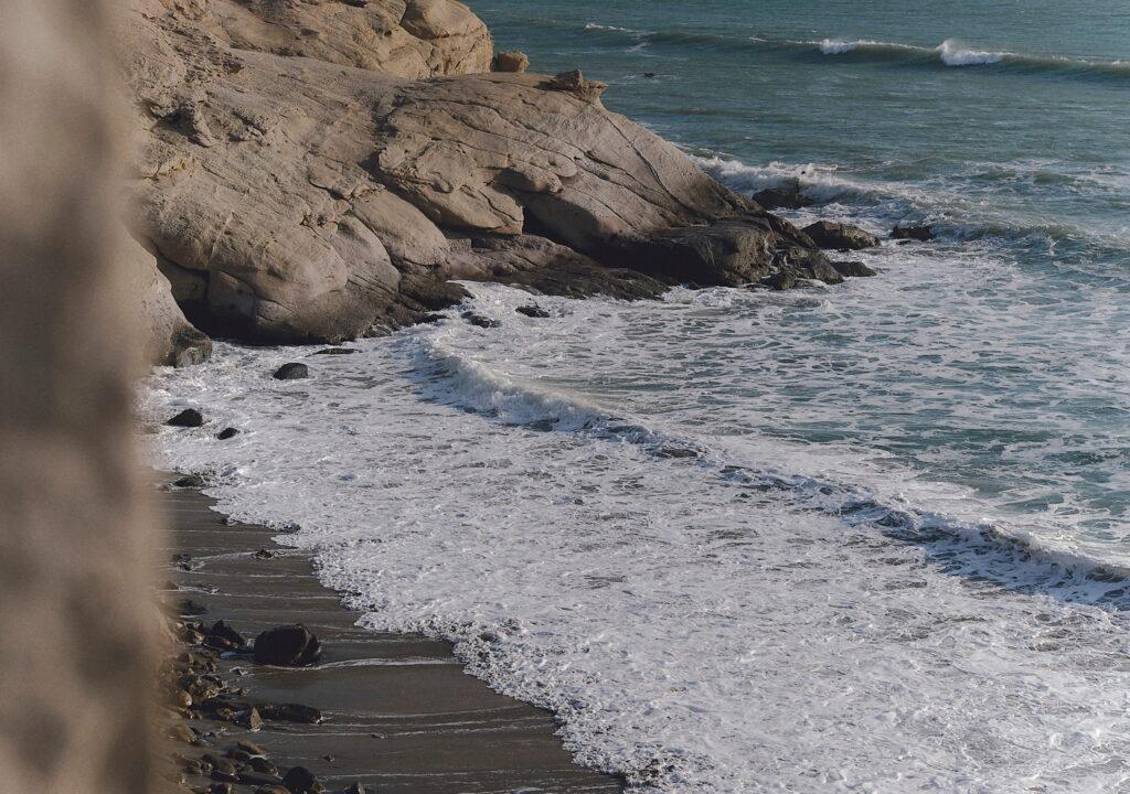 Felsige Küste, an der sich die Wellen an einem schmalen Sandstrand im Inkaterra Cabo Blanco in Peru brechen