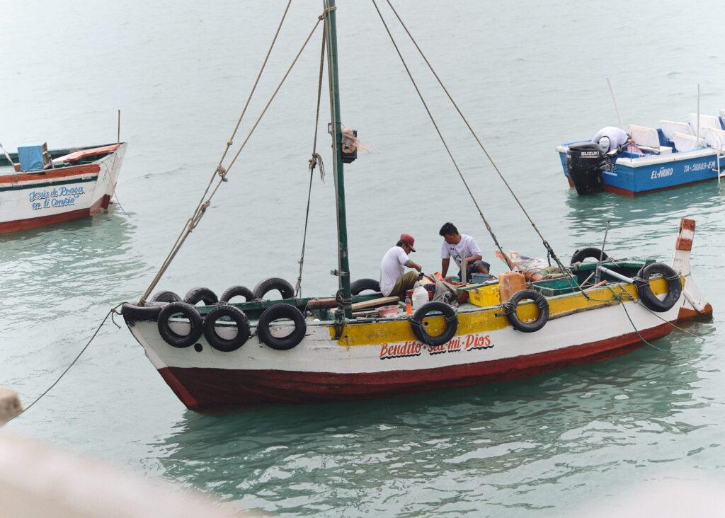 Ein kleines Fischerboot, an dem zwei Männer arbeiten, treibt auf ruhigem Wasser neben anderen Booten