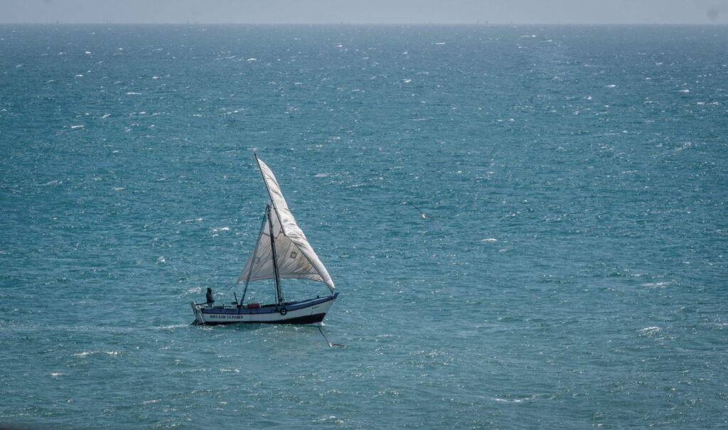 Ein kleines Segelboot mit einem einzigen weißen Segel auf ruhiger See unter klarem Himmel