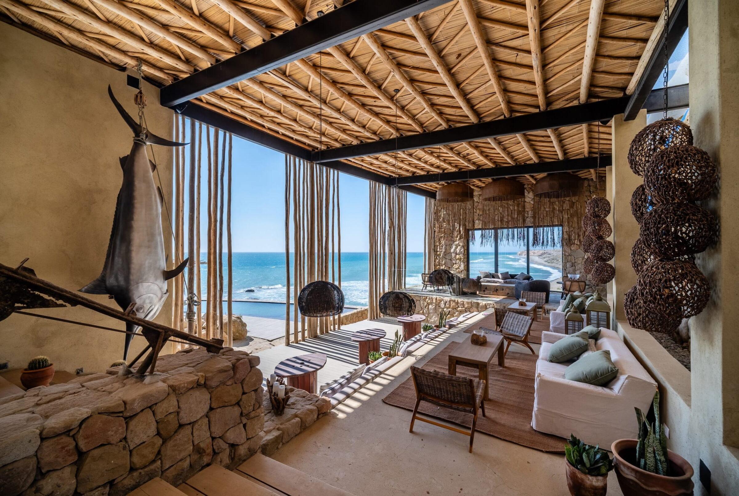 Lounge-Bereich im Freien mit geflochtener Decke, Steinwänden, hängenden Zierkugeln, Holzmöbeln und Meerblick im Inkaterra Cabo Blanco in Peru
