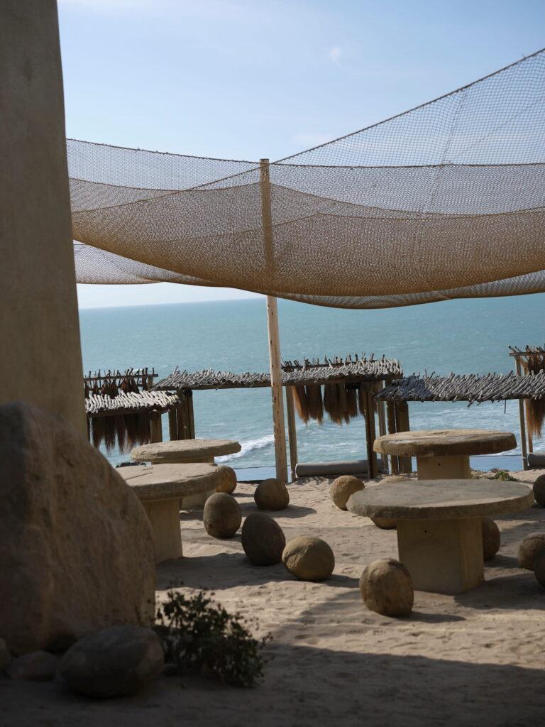 Lounge-Bereich im Freien mit runden Steintischen und Hockern unter einem großen Netzdach direkt am Meer im Inkaterra Cabo Blanco in Peru
