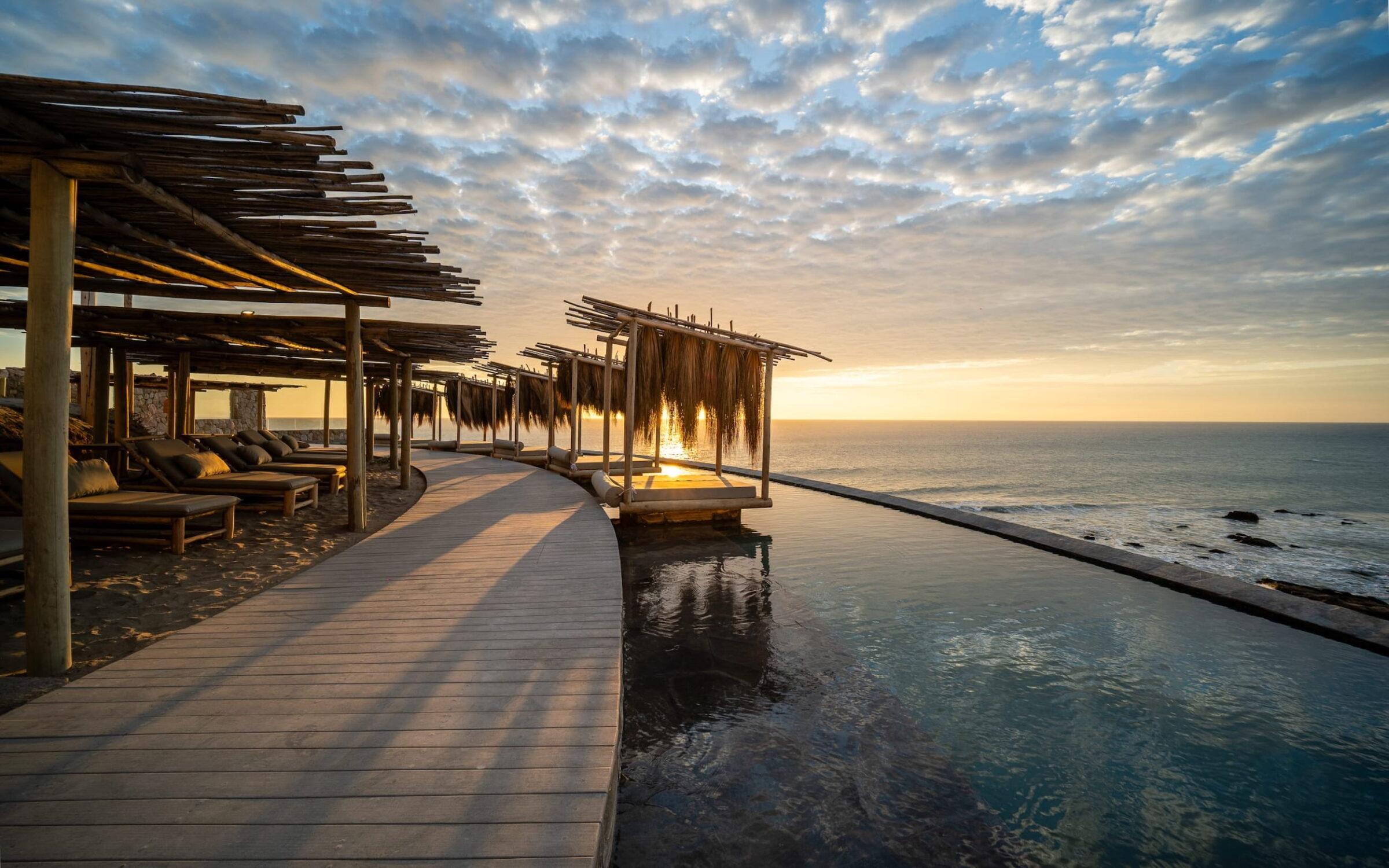 Pool neben einer Holzterrasse mit schattigen Liegen und Blick auf den Ozean bei Sonnenuntergang im Inkaterra Cabo Blanco in Peru