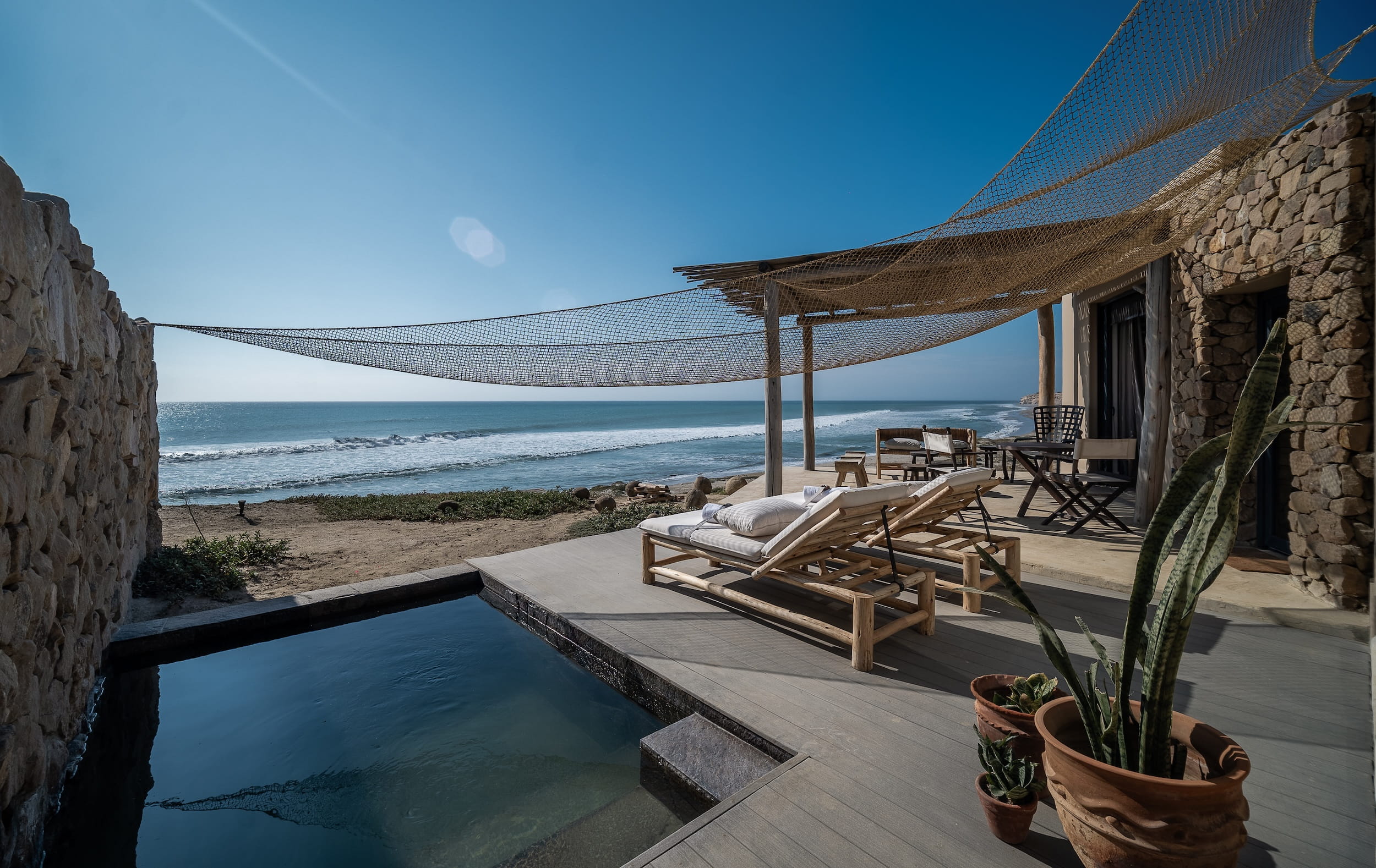 Terrasse mit Steinmauern, Holzliegestühlen, kleinem Pool, Topfpflanzen und einem Sonnenschirm mit Netz, mit Blick auf den Ozean / Suite im Inkaterra Cabo Blanco in Peru