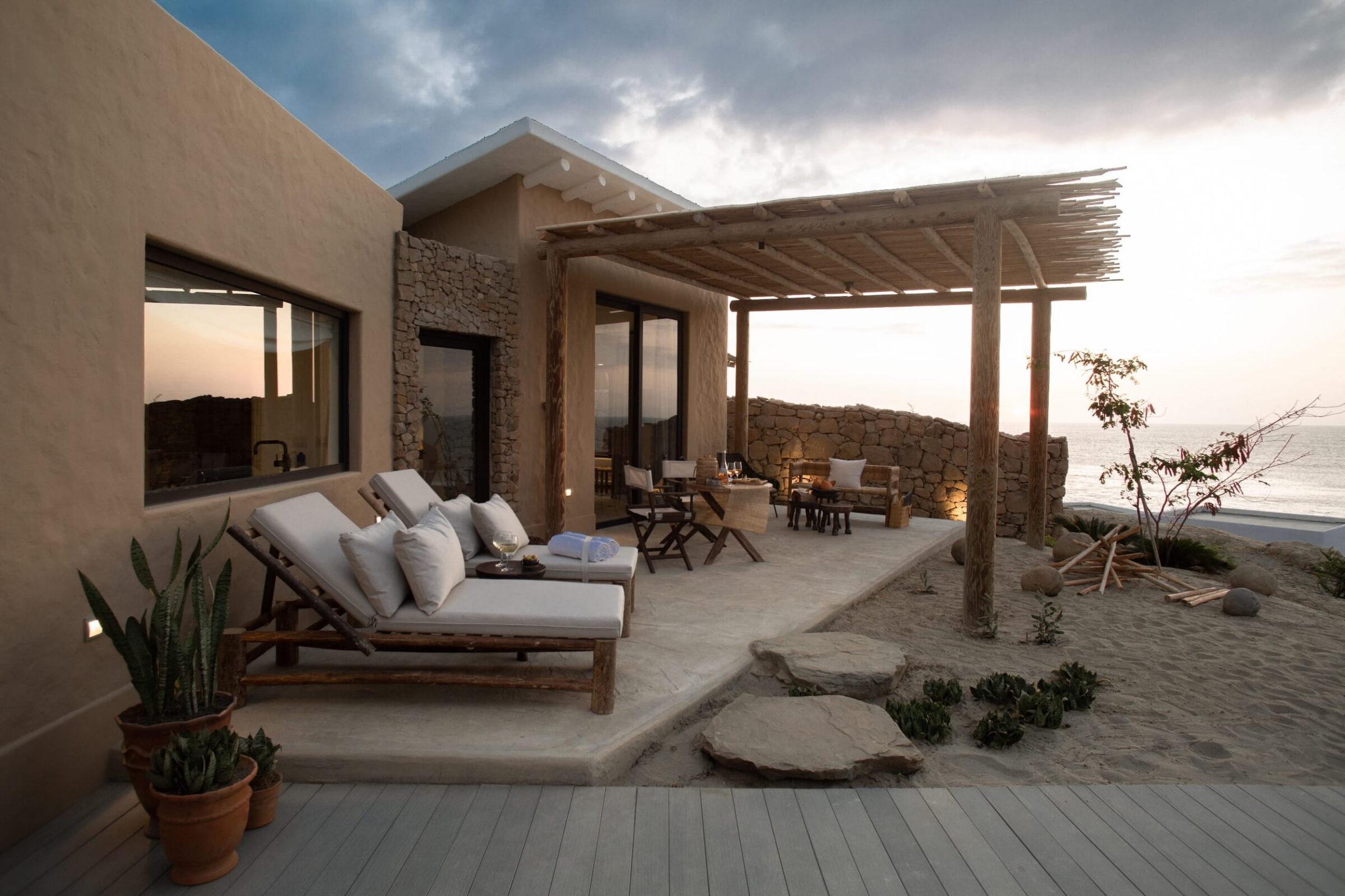 Außenbereich einer Küstensuite im Inkaterra Cabo Blanco mit Liegestühlen, einer Holzpergola, einer Steinmauer und Meerblick bei Sonnenuntergang