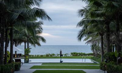 Eine Person, die in einer Yoga-Pose auf einer Plattform am Pool steht, während Palmen den Blick auf das Meer im Resort „The Anam Mui Ne“ in Vietnam einrahmen