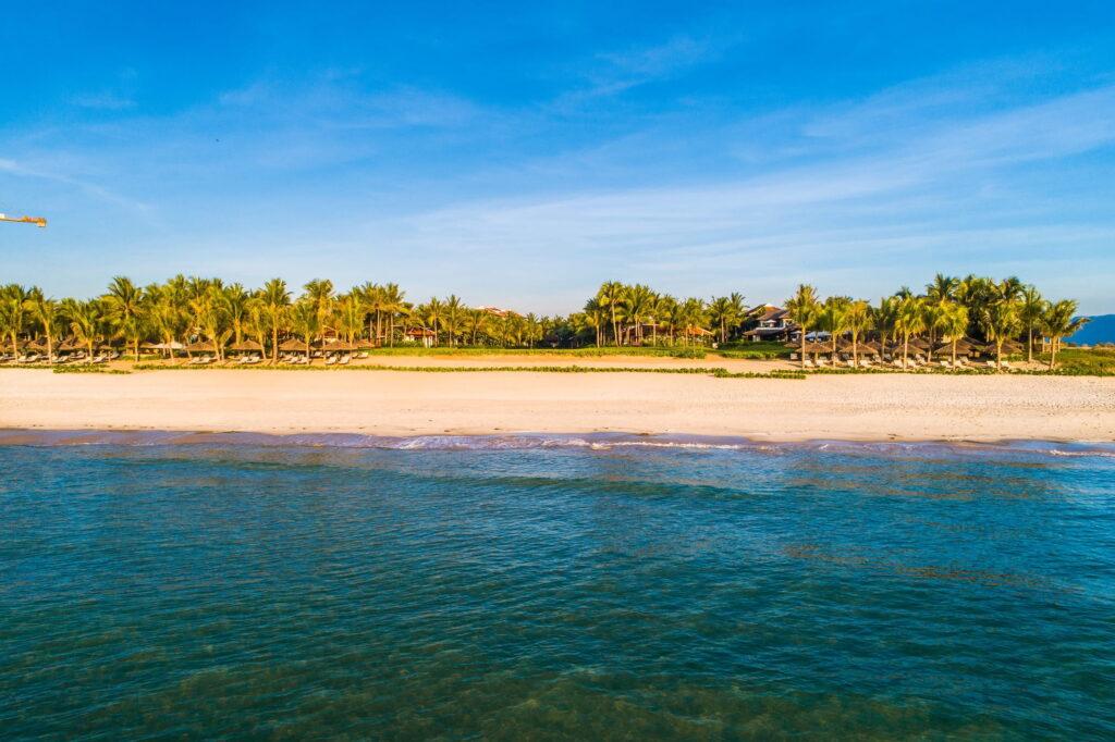 Strand mit Sandufer und Palmenreihen im Hintergrund im Resort „The Anam Cam Ranh“ in Vietnam