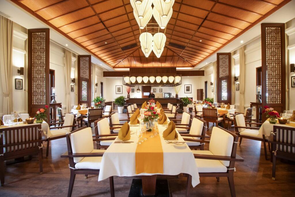 Luxuriöses Restaurant im The Anam Cam Ranh Resort mit hohen Holzdecken, großen Laternenlampen, elegant gedeckten Tischen und Holzmöbeln