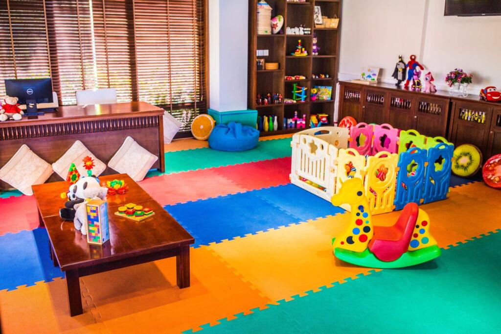 Kinderspielzimmer im „The Anam Cam Ranh“ mit bunten Schaumstoffmatten, einem Holztisch mit Spielzeug, einem kleinen, eingezäunten Spielbereich und Regalen mit Spielzeug und Büchern