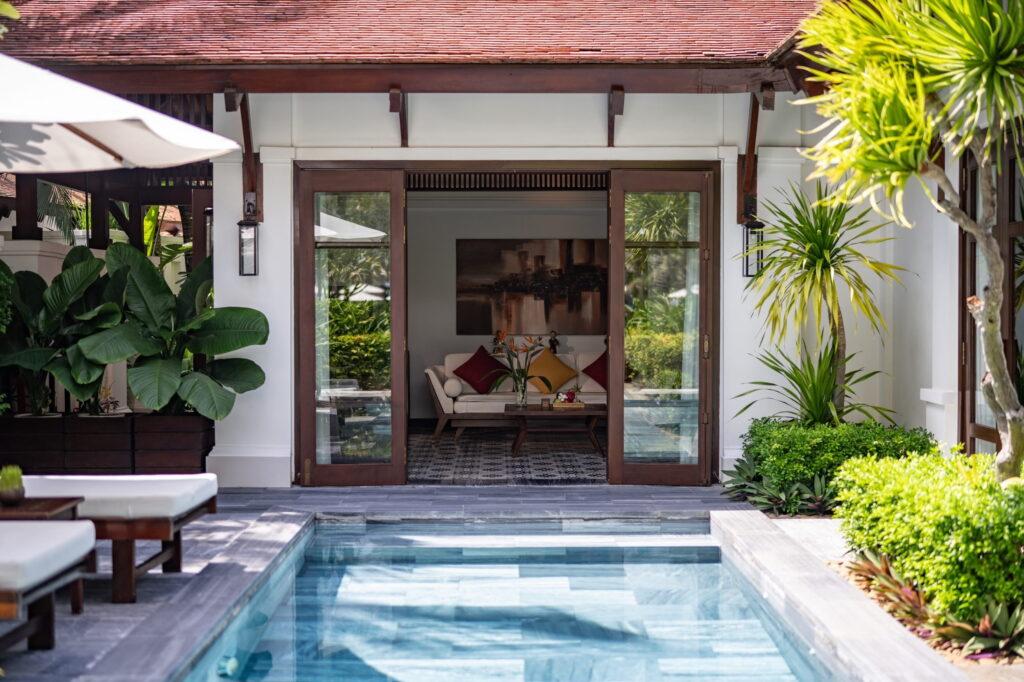 Ein Außenpool, der zum offenen Eingangsbereich der Villa führt, in dem ein Sofa und Kissen stehen – im Resort „The Anam Cam Ranh“