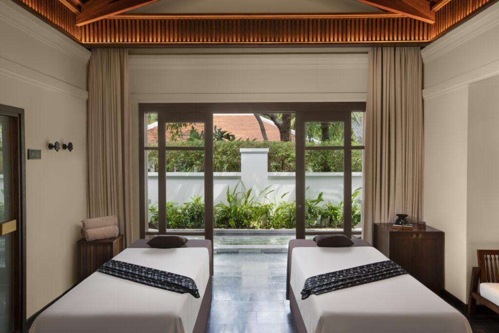 Behandlungsraum im „The Anam Spa“ mit zwei Massageliegen, die auf eine Glastür blicken, die zu einem Gartenbereich führt