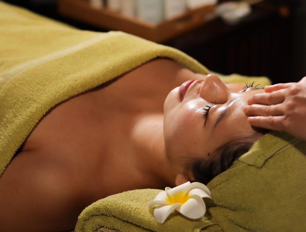 Eine Frau liegt entspannt mit geschlossenen Augen auf einer Liege im „The Anam Spa“ in Cam Ranh, Vietnam; neben ihrem Kopf liegen ein Handtuch und eine Blume.