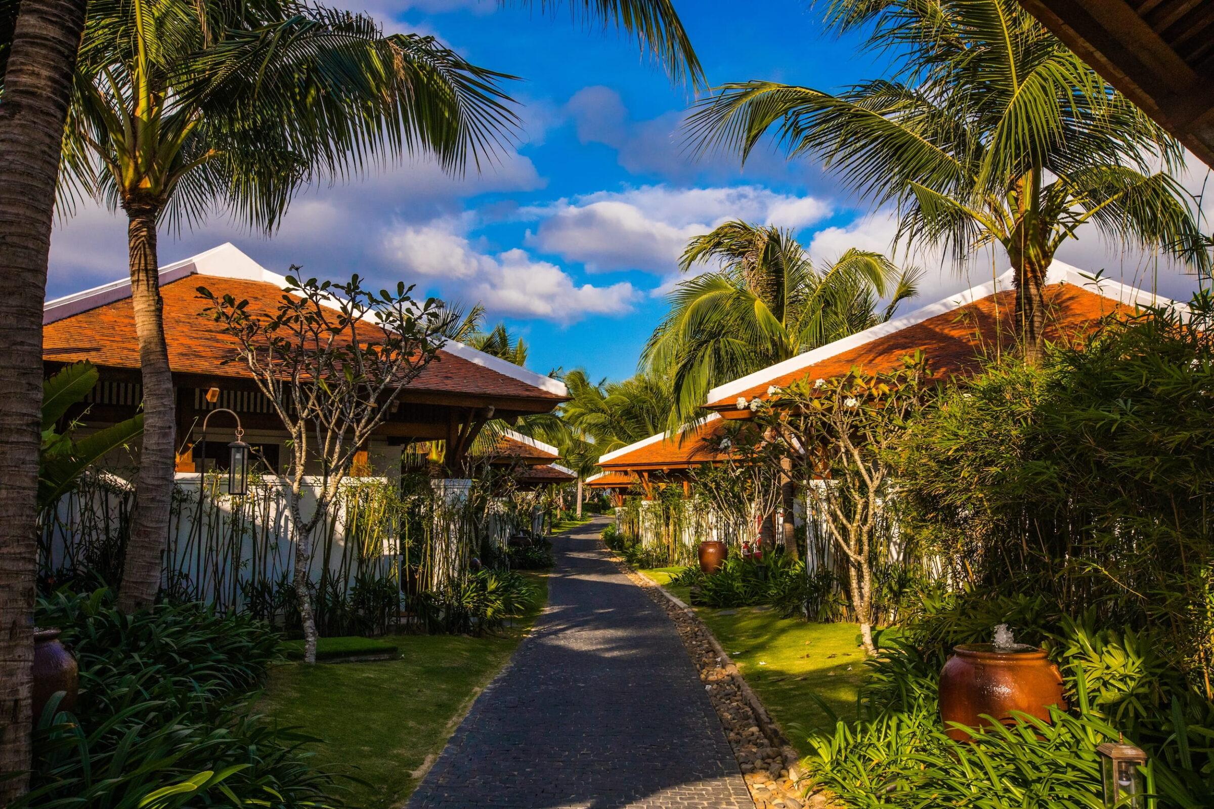 Gepflasterter Weg zwischen Bungalows mit roten Dächern und Palmen im Resort „The Anam Cam Ranh“ in Vietnam