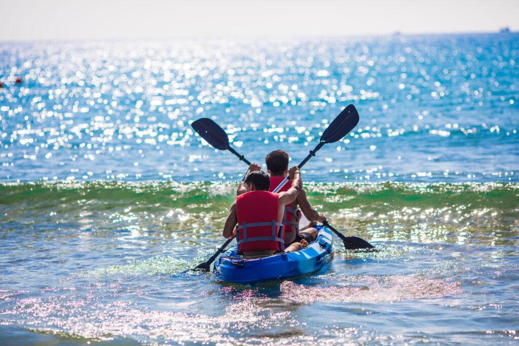 Zwei Leute in Schwimmwesten, die in einem blauen Kajak auf ruhigem Meerwasser paddeln, während sich das Sonnenlicht auf der Wasseroberfläche spiegelt