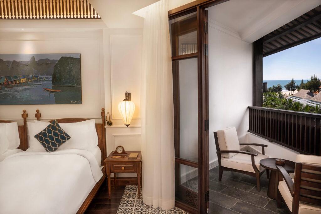 Eine Ecke im Hotelzimmer im „The Anam Mui Ne“ mit einem Schreibtisch und einem Stuhl aus Holz am Fenster, einem an der Wand montierten Flachbildfernseher und einem Schrank mit Kaffeemaschine und Glasflaschen