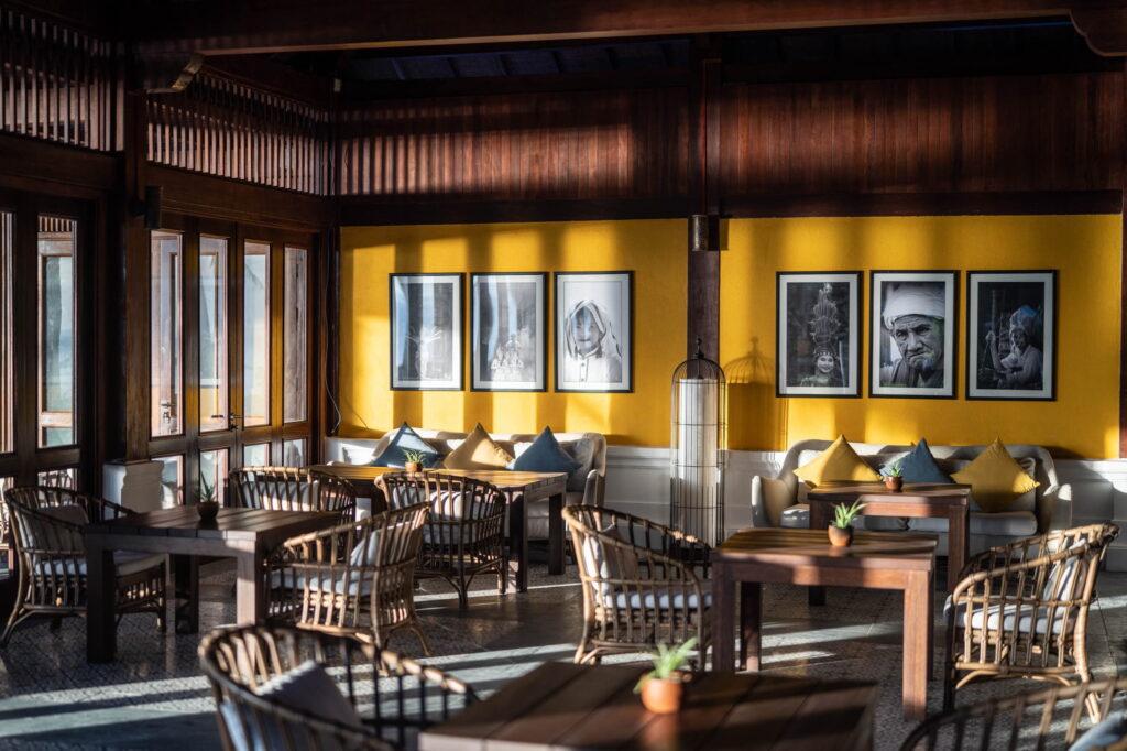 Der Innenraum des Restaurants „Lang Viet“ im „The Anam Mui Ne“ mit Holztischen und Korbstühlen, die vor einer gelben Wand mit gerahmten Schwarz-Weiß-Porträts stehen