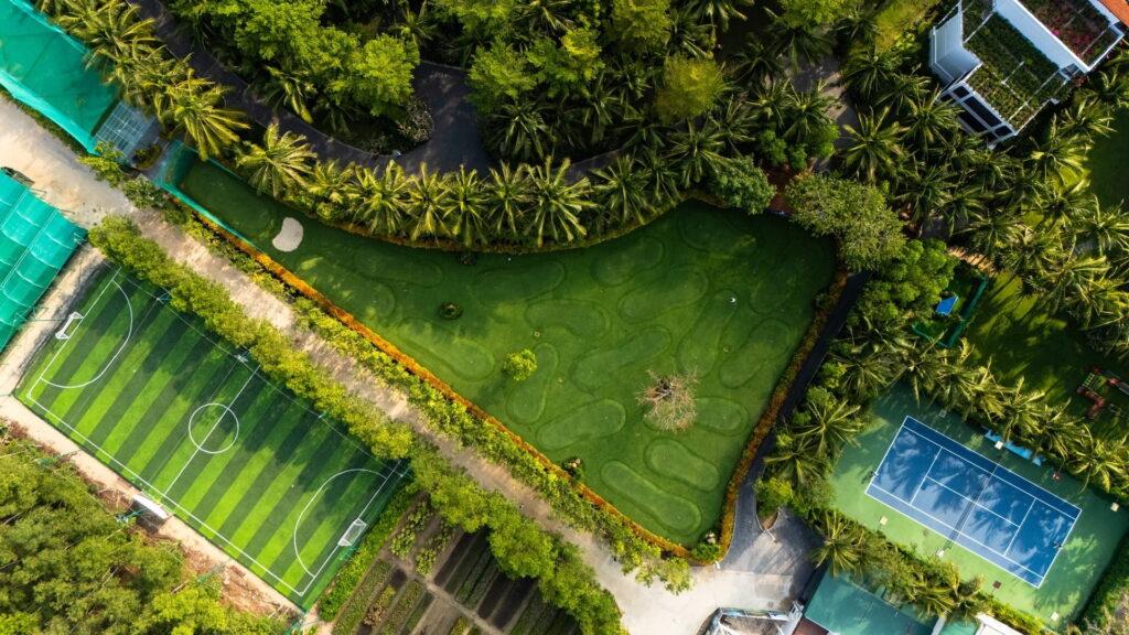 Luftaufnahme eines Minigolfplatzes neben einem Fußballfeld und einem Tennisplatz, umgeben von tropischer Vegetation, im luxuriösen Resort „The Anam Cam Ranh“ in Vietnam