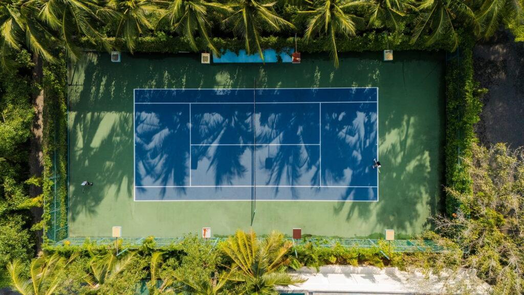 Luftaufnahme eines Tennisplatzes, umgeben von Palmen und dichter Vegetation, im „The Anam Cam Ranh Resort“ in Vietnam