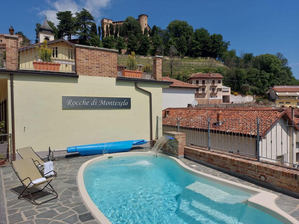 Kleiner Pool mit Wasserfall bei den Ferienwohnungen „Rocche di Montexelo“, vor der Kulisse eines Hügels mit einer Burg und weiteren Gebäuden