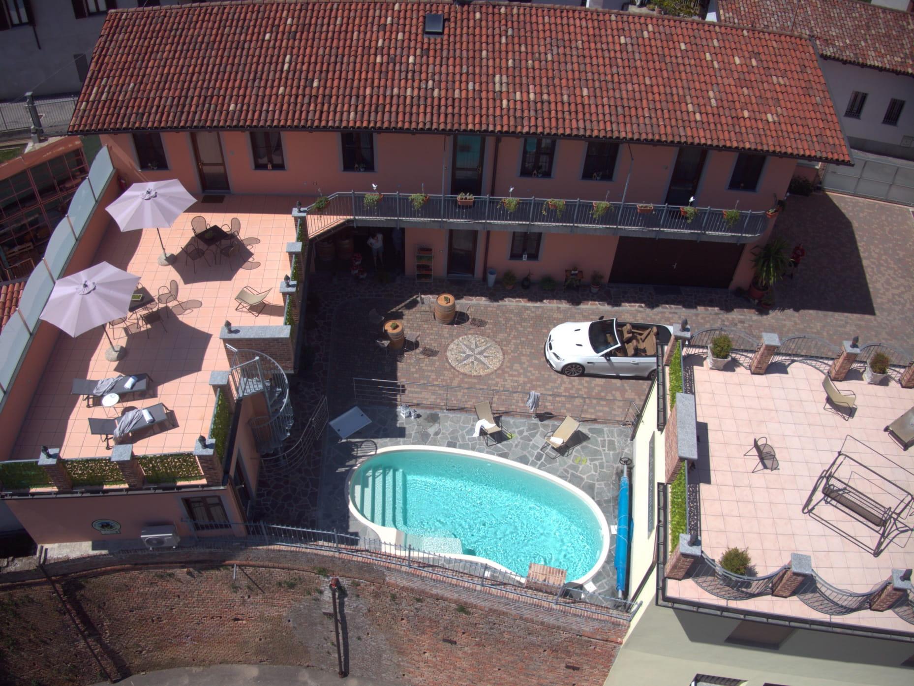 Luftaufnahme der Ferienwohnungen „Rocche di Montexelo“ mit Pool, Terrasse, Sonnenschirmen, Sitzgelegenheiten und einem weißen Auto im Innenhof