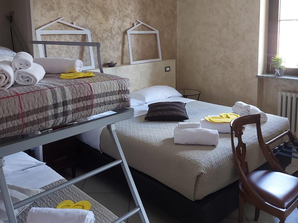 Ein schlicht eingerichtetes Schlafzimmer in den Ferienwohnungen „Rocche di Montexelo“ mit einem Doppelbett, einem Etagenbett, Holzmöbeln und Handtüchern auf den Betten