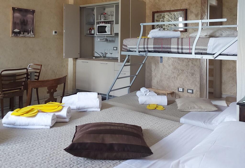 Zimmer in der Ferienwohnung „Rocche di Montexelo“ mit einem Etagenbett, einem Doppelbett, einem Tisch mit Stühlen, einer kleinen Kochnische und Handtüchern