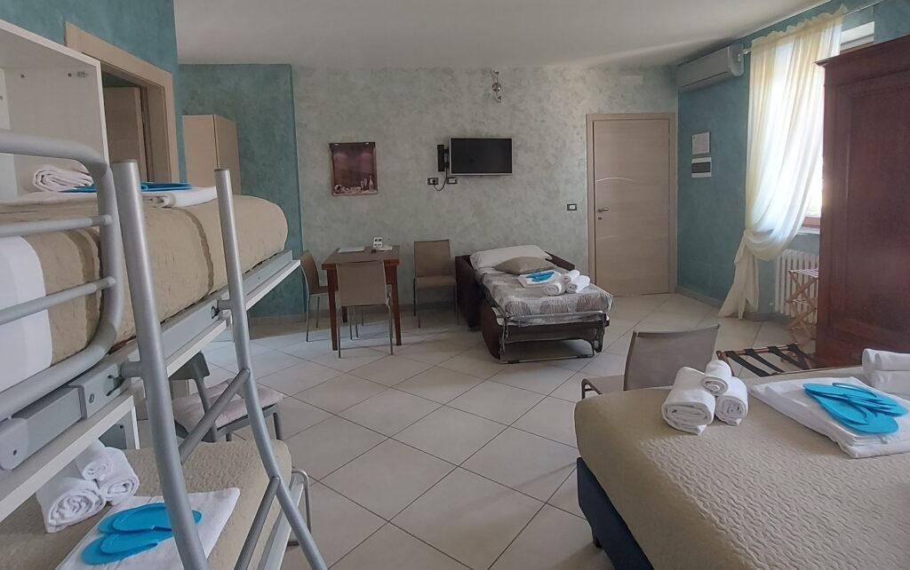 Zimmer in einer Ferienwohnung in Rocche di Montexelo mit einem Etagenbett, einem Einzelbett, einem Doppelbett, einem Schreibtisch, einem an der Wand montierten Fernseher und einem Fenster mit Vorhang